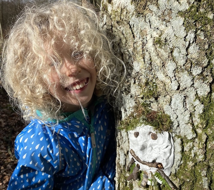 Child standing next to clay face on tree
