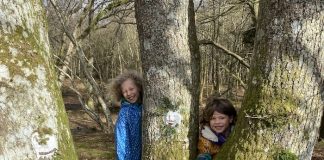 Two children with clay faces on tree trunk