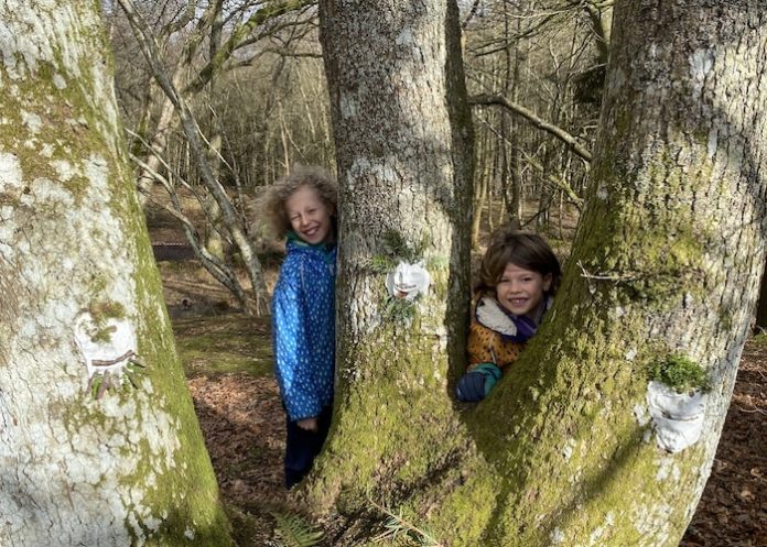 Two children with clay faces on tree trunk