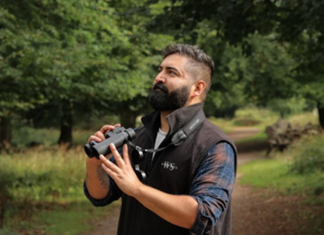 Featured Bird Watcher: Wilderskies Nick Patel/ @wilderskies with binoculars in a forrest looking for birds.