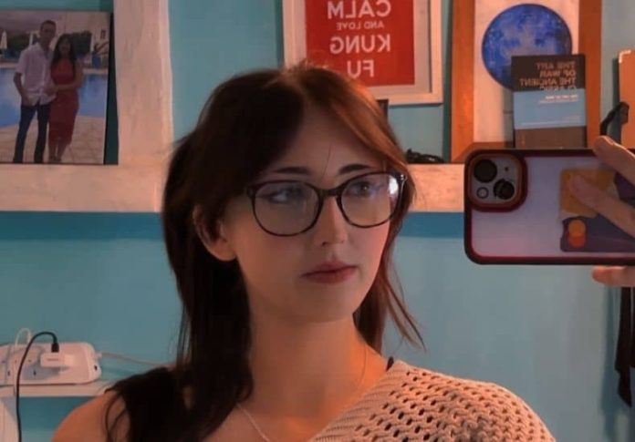 woman-in-room Mirror selfie of a young woman with shoulder-length dark hair and glasses wearing a neutral knit top in a bright room.